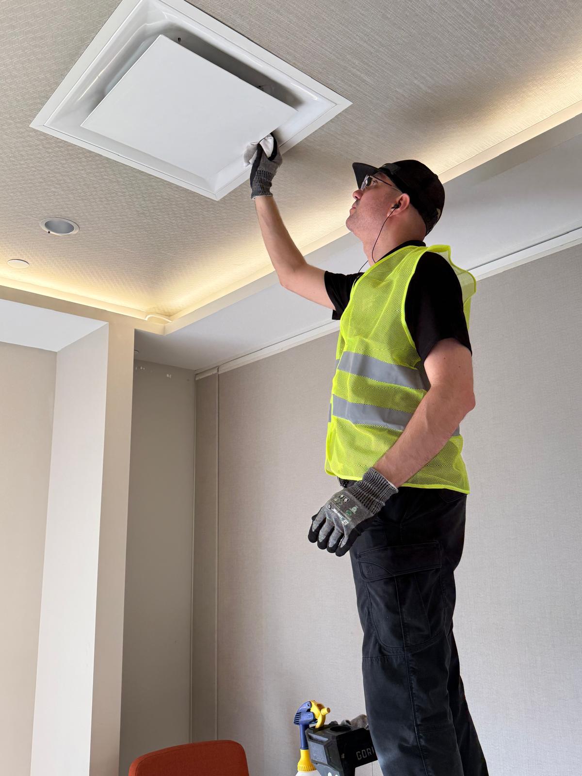 Technician wiping a ceiling supply diffuser after commercial duct cleaning
