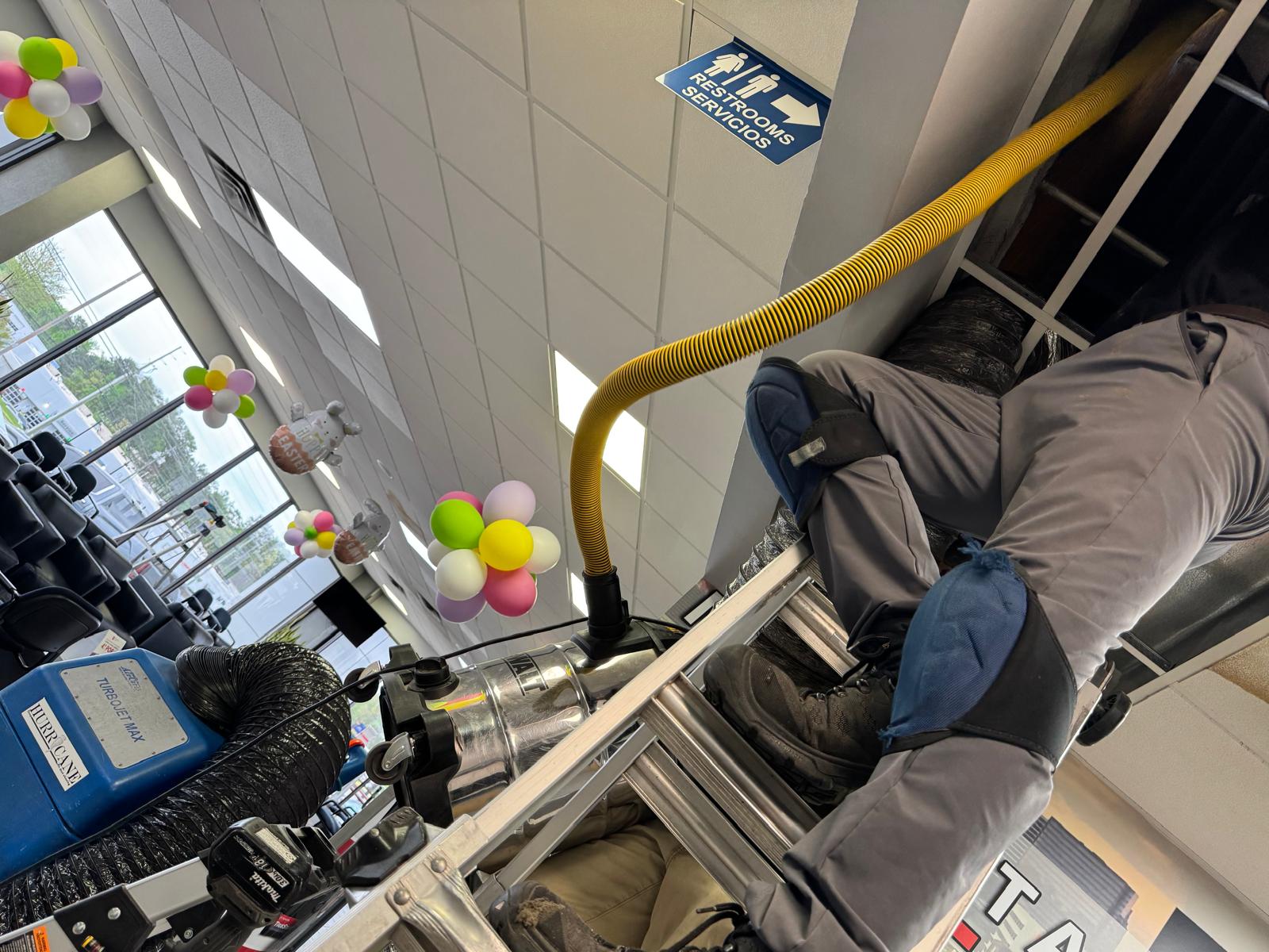 Dealership corridor — knee-pad ladder work near restroom signage