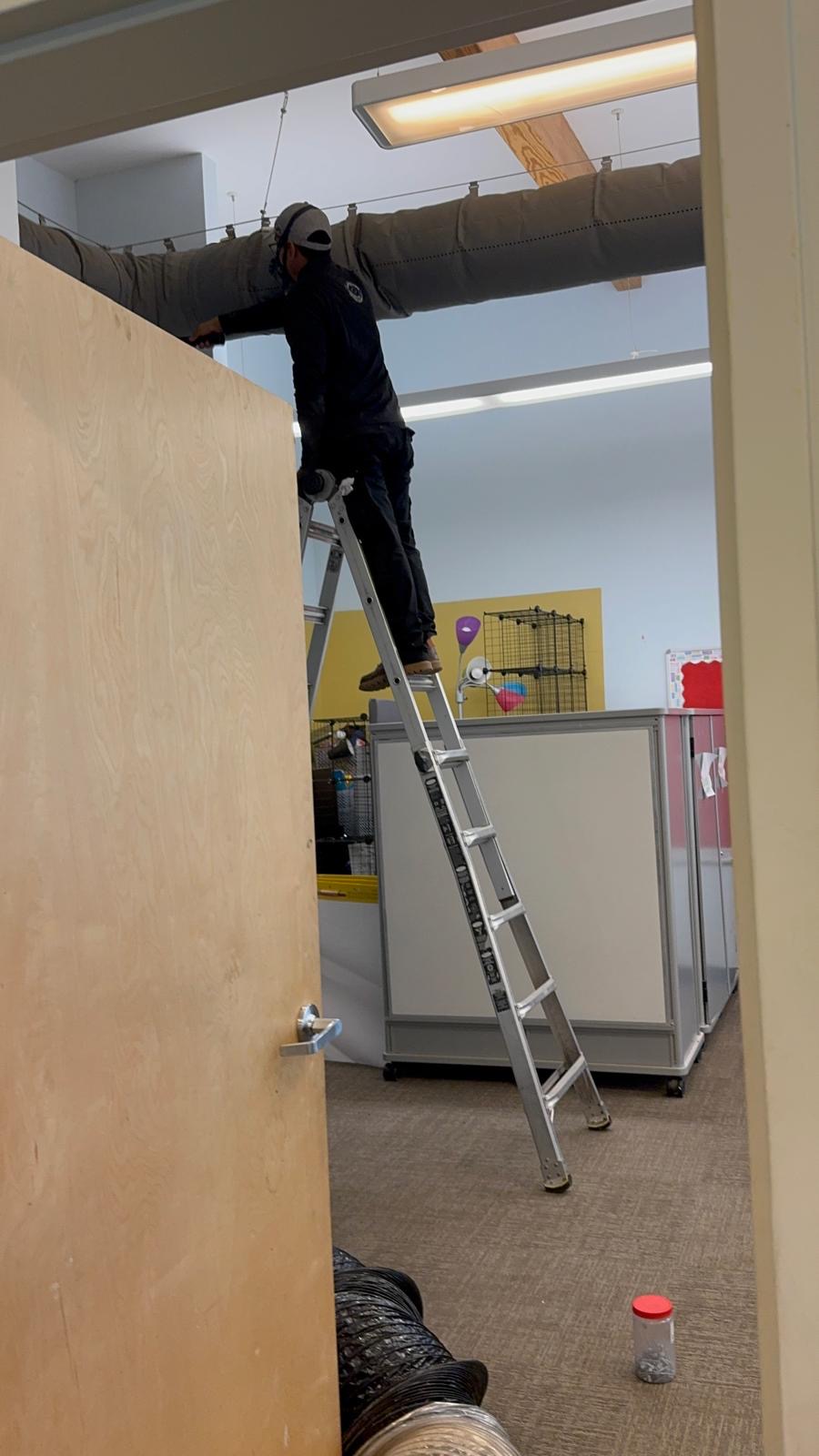 Technician servicing an insulated ceiling duct run inside a commercial building