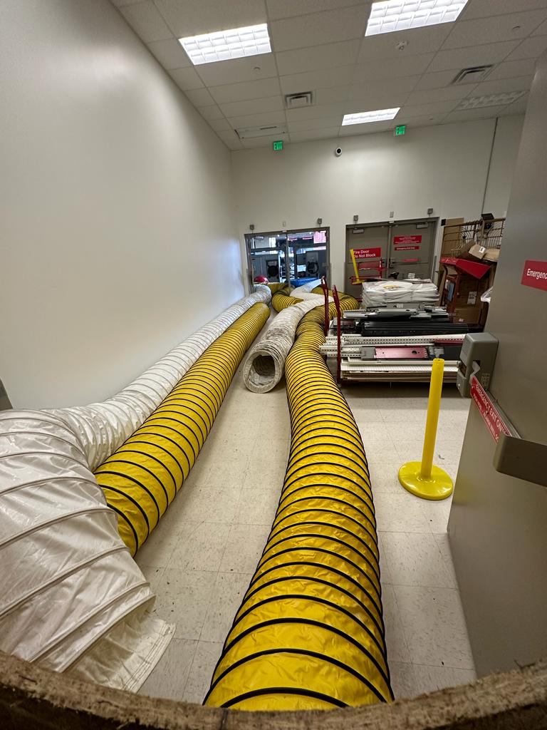 Big-box back-of-house — dual flex duct runs feeding negative-air machines through emergency exit