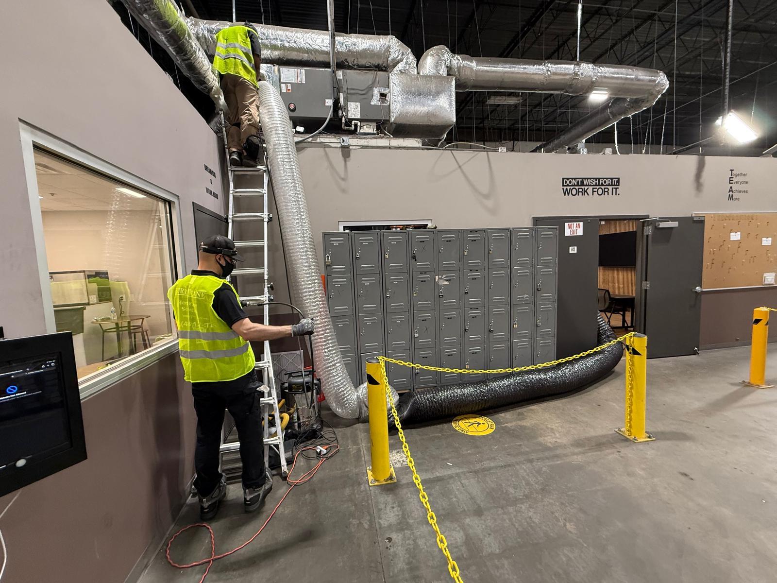 Warehouse facility — dual-tech crew cleaning rooftop unit supply lines above the locker area