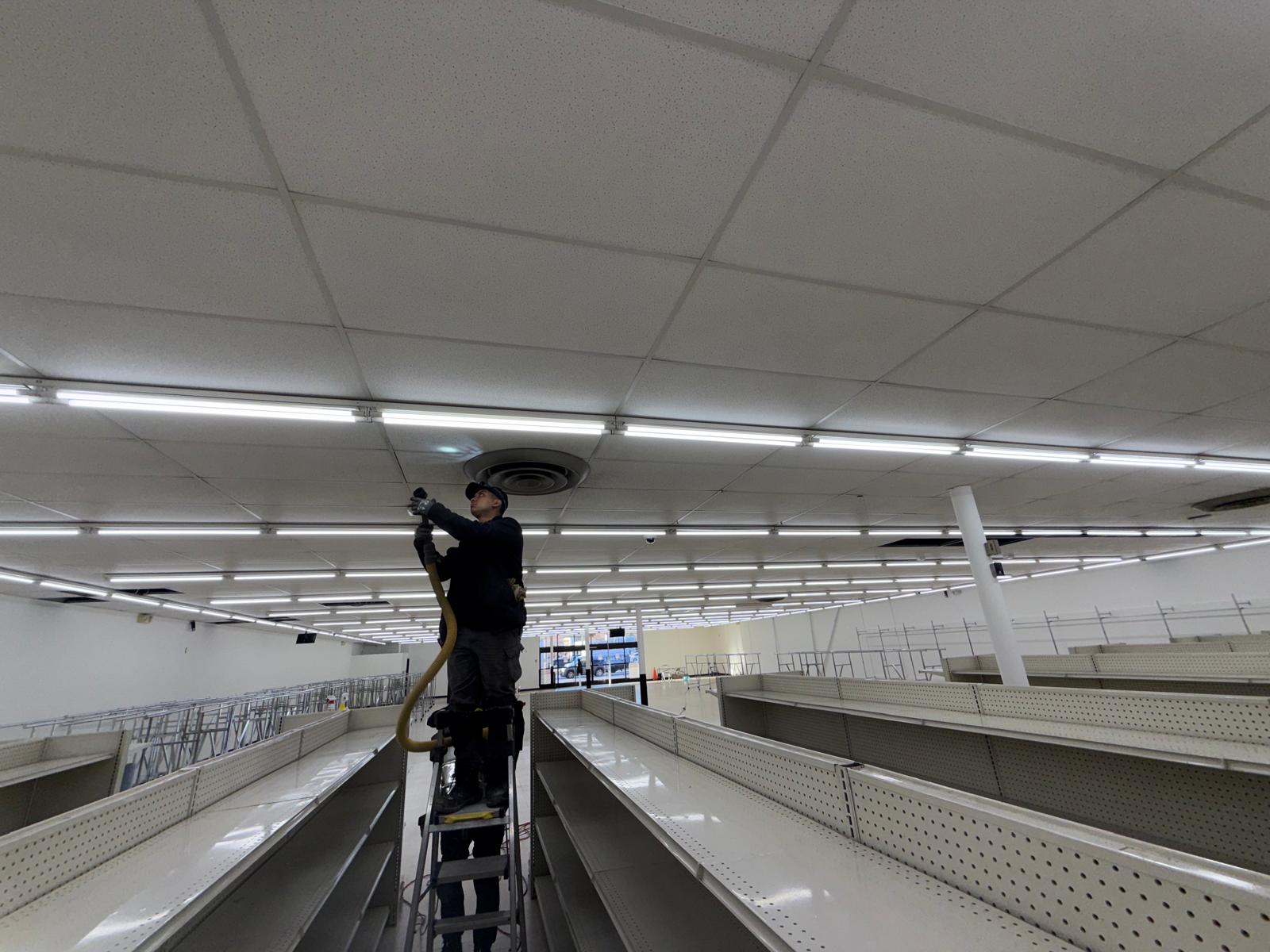 Retail sales floor — ceiling diffuser cleaning above empty shelving aisles