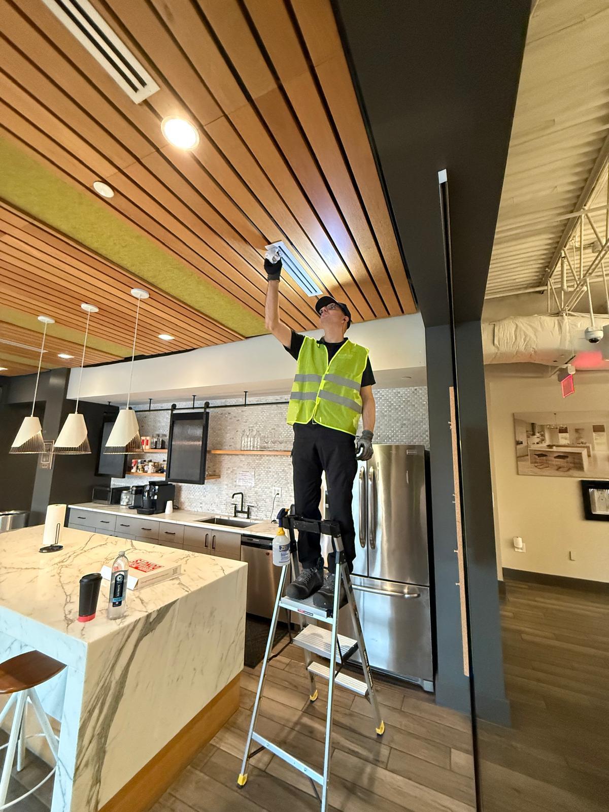 Technician cleaning a linear ceiling vent in an office break room