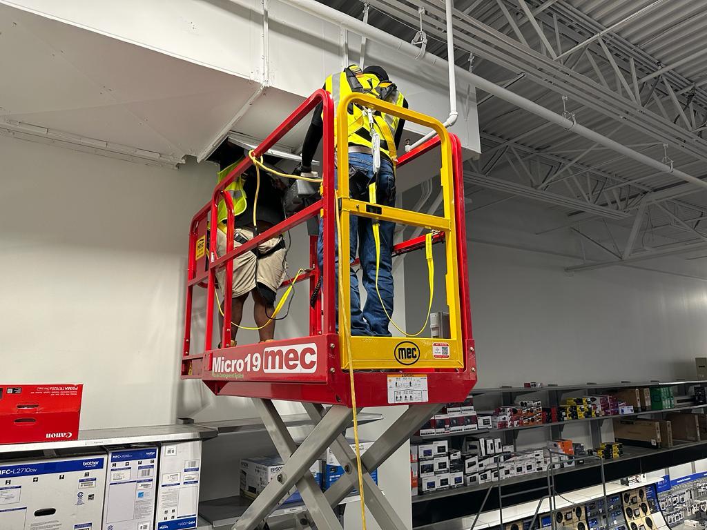 Electronics showroom — fall-protection harness work above retail shelving