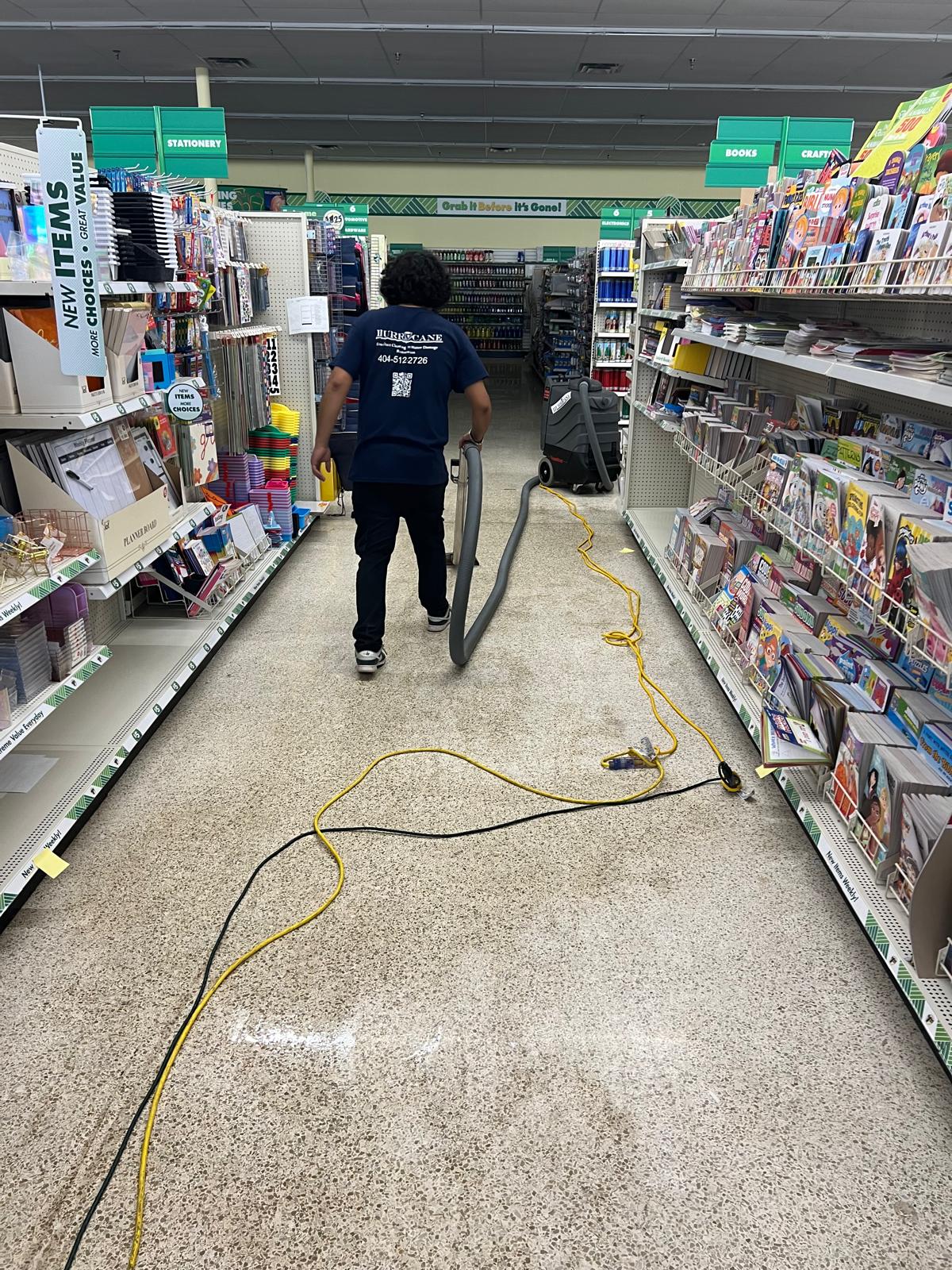 Dollar Tree water damage cleanup — extraction wand and hose pulling standing water from the books and crafts aisle