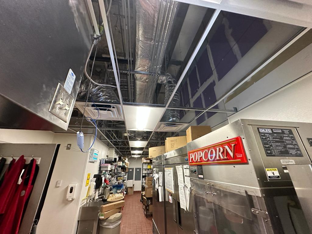 Commercial kitchen — ceiling tile pulled for supply duct inspection above prep line